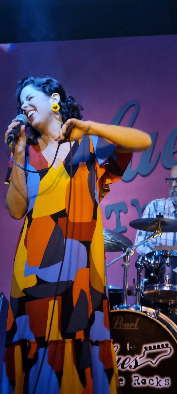 Carol Nogueira cantando ao vivo, em vestido colorido